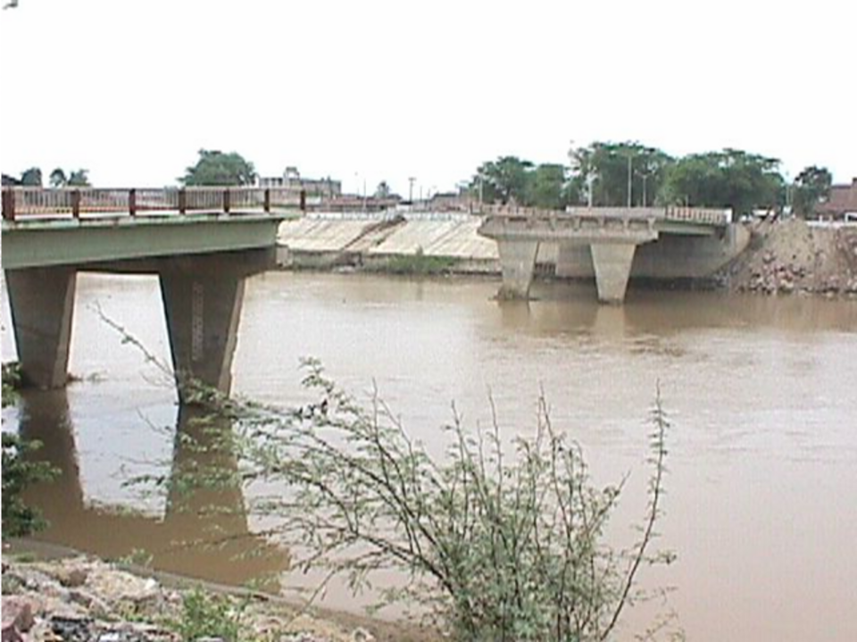 El antiguo puente Bolognesi de Piura con su tramo central derrumbado sobre el río crecido.